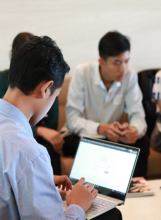 Businessman using a laptop in a collaborative workspace, with team members in the background